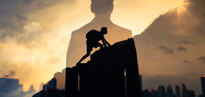Silueta de un hombre de espaldas superpuesta a una silueta de hombre subiendo una montaña