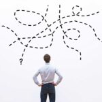 10 mitos y realidades del emprendimiento que debes conocer Hombre de espaldas mira hacia una pared blanca en donde hay líneas punteadas e interrogantes