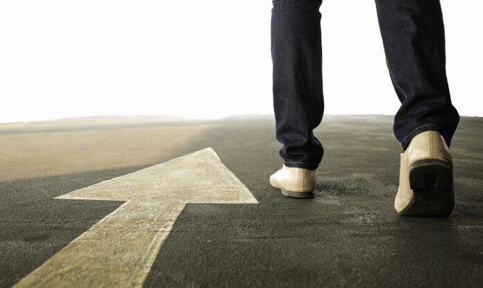 flecha en el suelo y piernas caminando al lado, señalan el camino correcto hacia las historias de personas exitosas