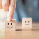 Importancia del servicio al cliente | 10 razones para mejorarlo Mano elige bloque de madera con cara sonriente debido a la importancia del servicio al cliente