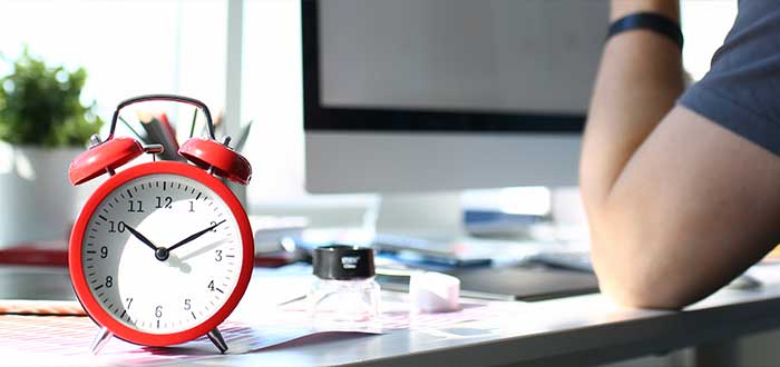 Persona trabajando sobre un escritorio con un reloj que simboliza su horario de trabajo